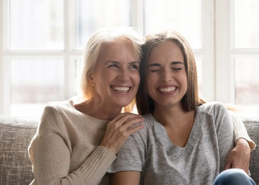 Adult Adoption - Older women hugging younger adult women on a couch. Both women are smiling. - bloomington il